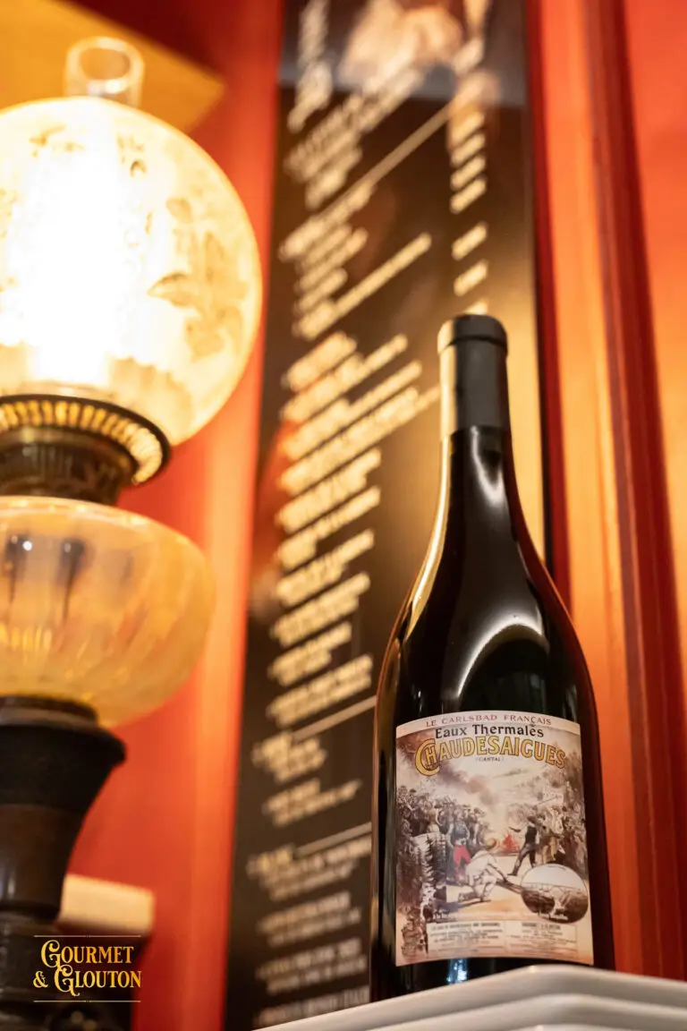 Bouteille « Eaux Thermales de ChaudesAigues » photographiée sur une table du restaurant Gourmet & Glouton, avec une étiquette inspirée d’une affiche ancienne.