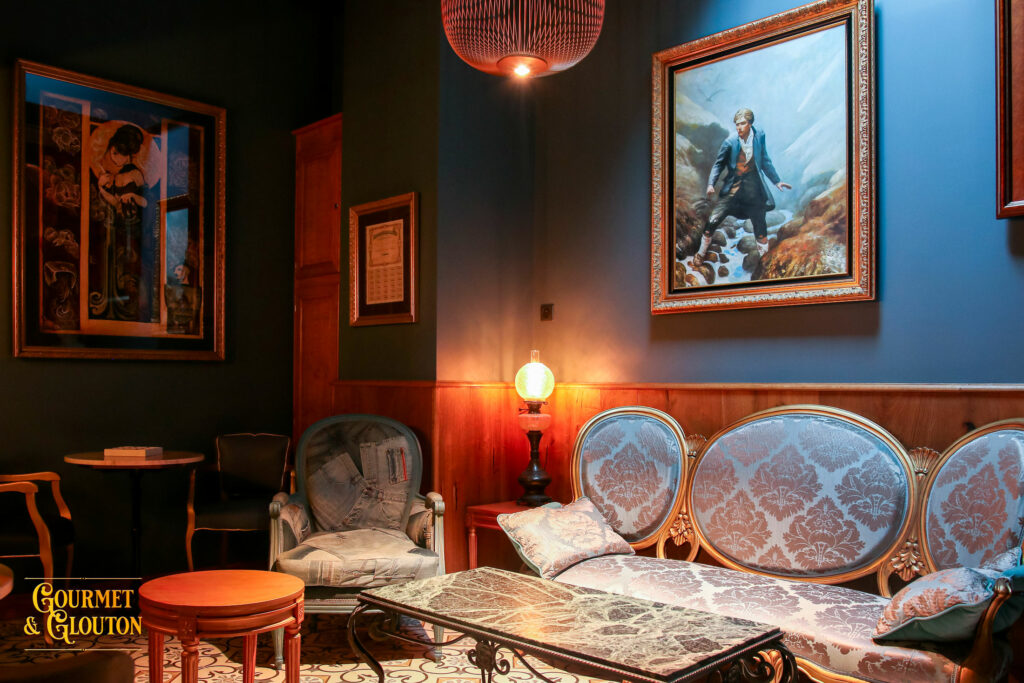 Salon Bleu du restaurant Gourmet & Glouton à Chaudes-Aigues, avec fauteuils anciens, tableaux, éclairage chaleureux et décor élégant.
