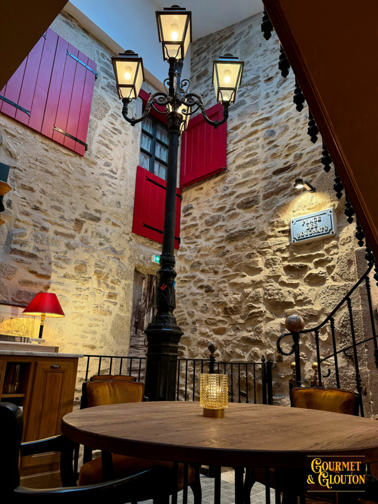 Vue intérieure montrant pierre brute, lampadaire et volets rouges ouverts.