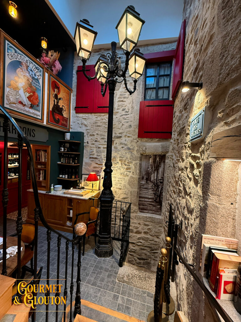 Vue intérieure montrant pierre brute, lampadaire et volets rouges ouverts.