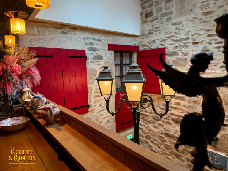 Vue intérieure montrant pierre brute, lampadaire et volets rouges ouverts.