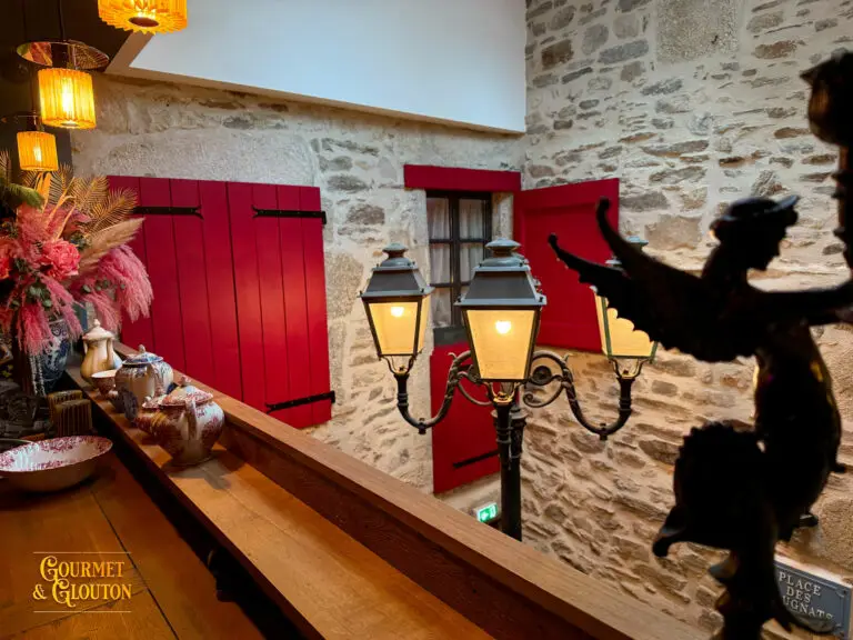 Vue intérieure montrant pierre brute, lampadaire et volets rouges ouverts.