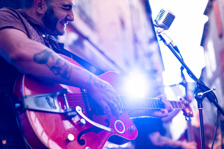 Musicien jouant de la guitare électrique devant un micro vintage lors d’un concert en terrasse chez Gourmet & Glouton à Chaudes-Aigues.