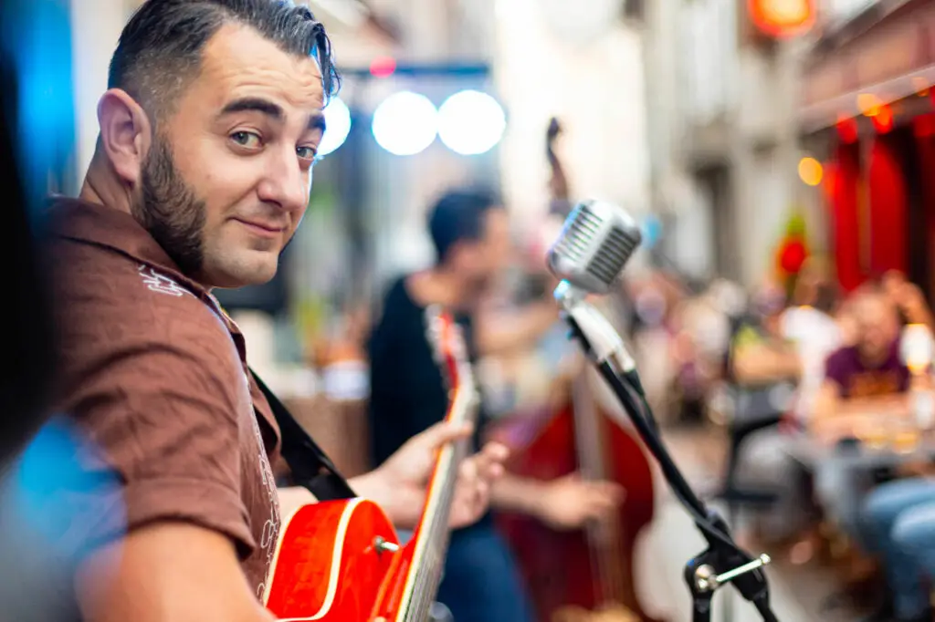 Musicien tenant une guitare et regardant le public devant un micro vintage lors d’un concert en terrasse chez Gourmet & Glouton à Chaudes-Aigues.