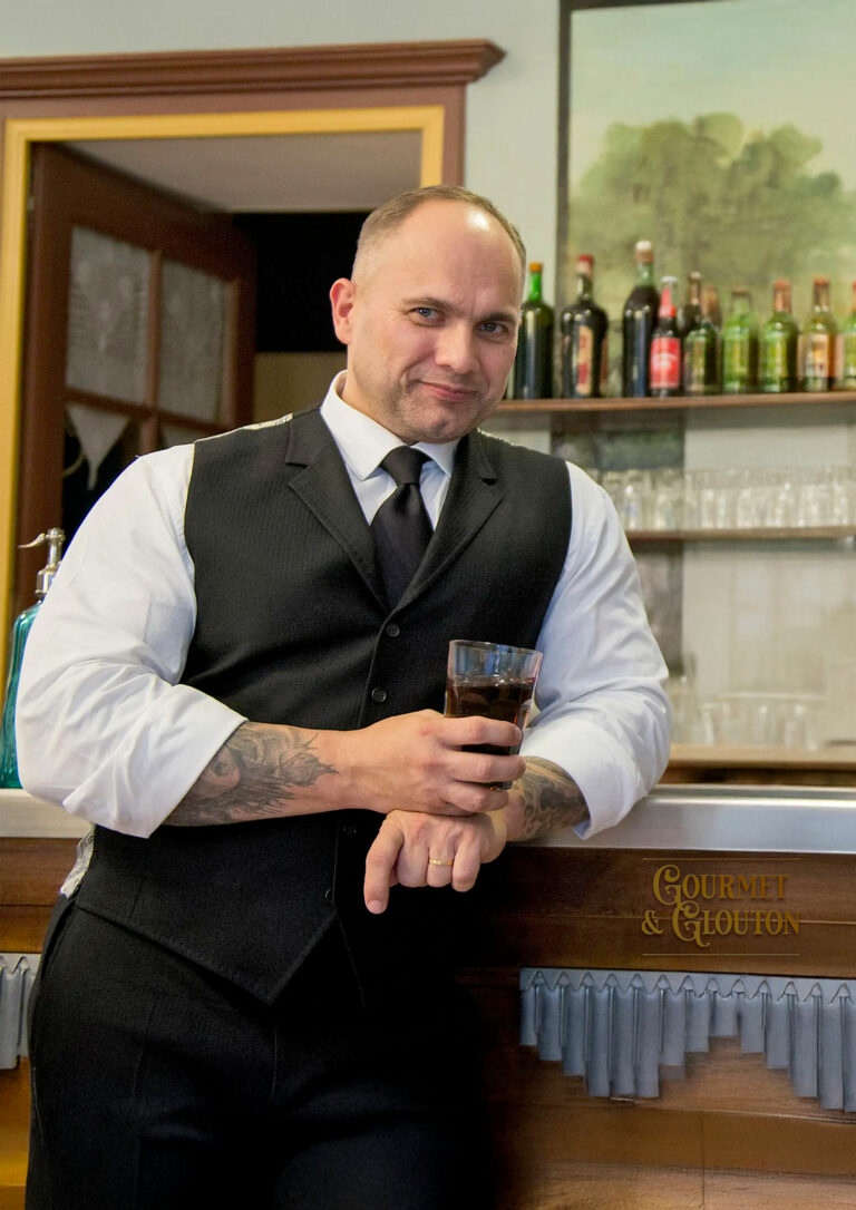 Stéphane Chaudesaigues, aubergiste et tatoueur, au comptoir de Gourmet & Glouton à Chaudes-Aigues, incarnant l’esprit bougnat de l’accueil, du lieu tenu dans la durée et du plaisir de recevoir