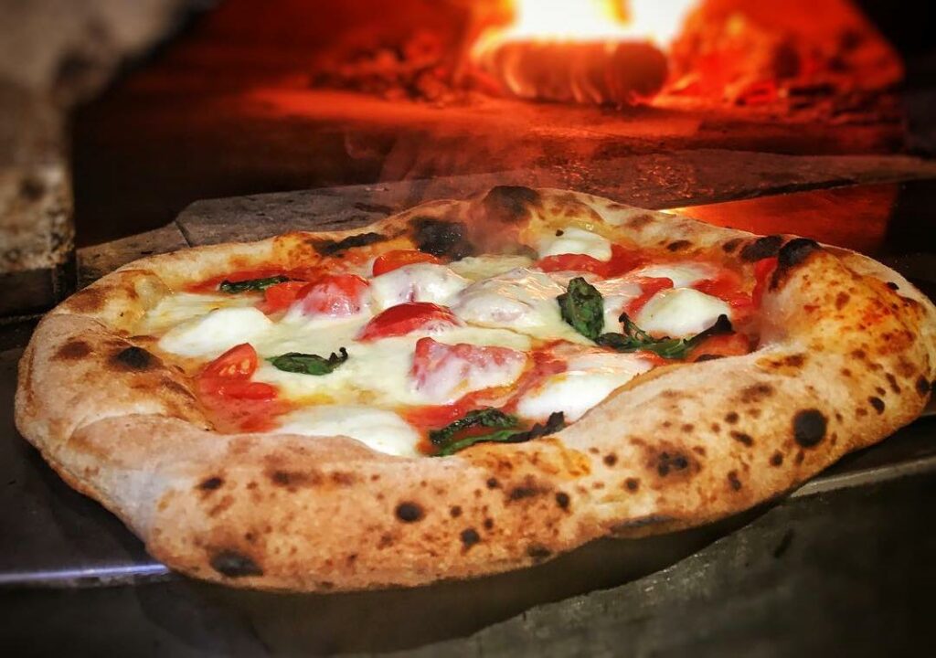 Pizza napolitaine cuite au feu de bois avec mozzarella et basilic dans un four à bois à Chaudes-Aigues