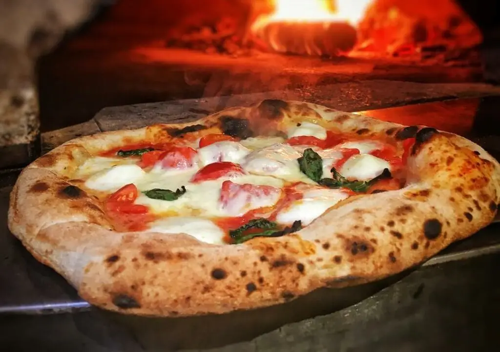 Pizza napolitaine cuite au feu de bois avec mozzarella et basilic dans un four à bois à Chaudes-Aigues