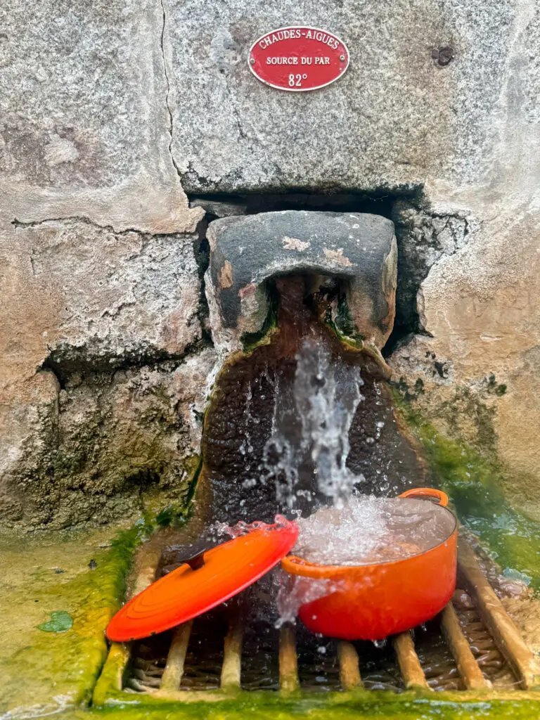 Casserole contenant plusieurs œufs sous le trop-plein de la Source du Par à Chaudes-Aigues pour une cuisson grâce à l'eau chaude naturelle à 82 °C.