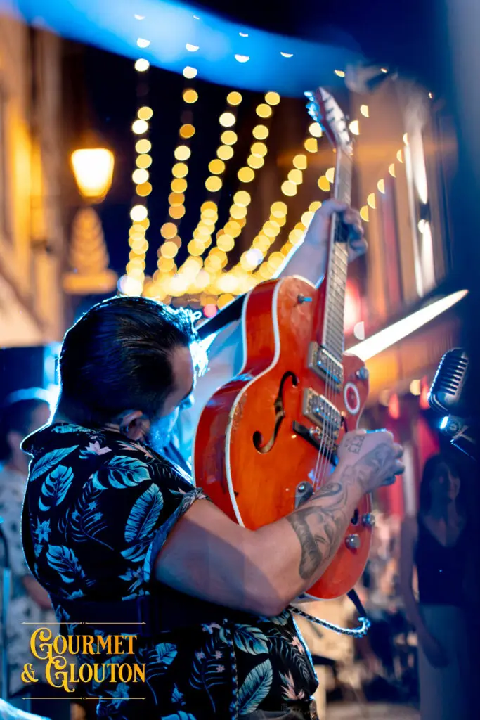 Guitariste de Wild Karma levant sa guitare sous les guirlandes des Terrasses Musicales de Chaudes-Aigues.