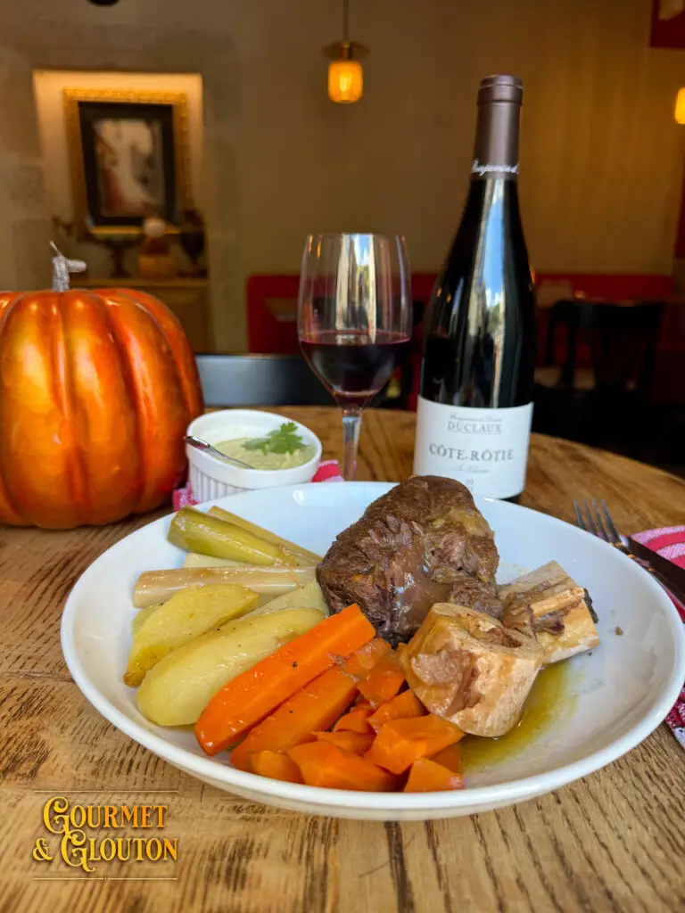 Assiette de pot-au-feu maison avec légumes, os à moelle, verre de vin et bouteille de Côte-Rôtie chez Gourmet & Glouton.