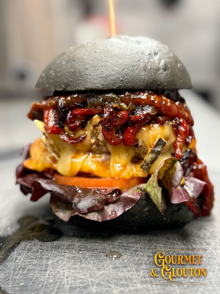 Burger Noir Charbon en gros plan, au pain noir, avec fromage fondu, galette de pomme de terre, tomate et salade.