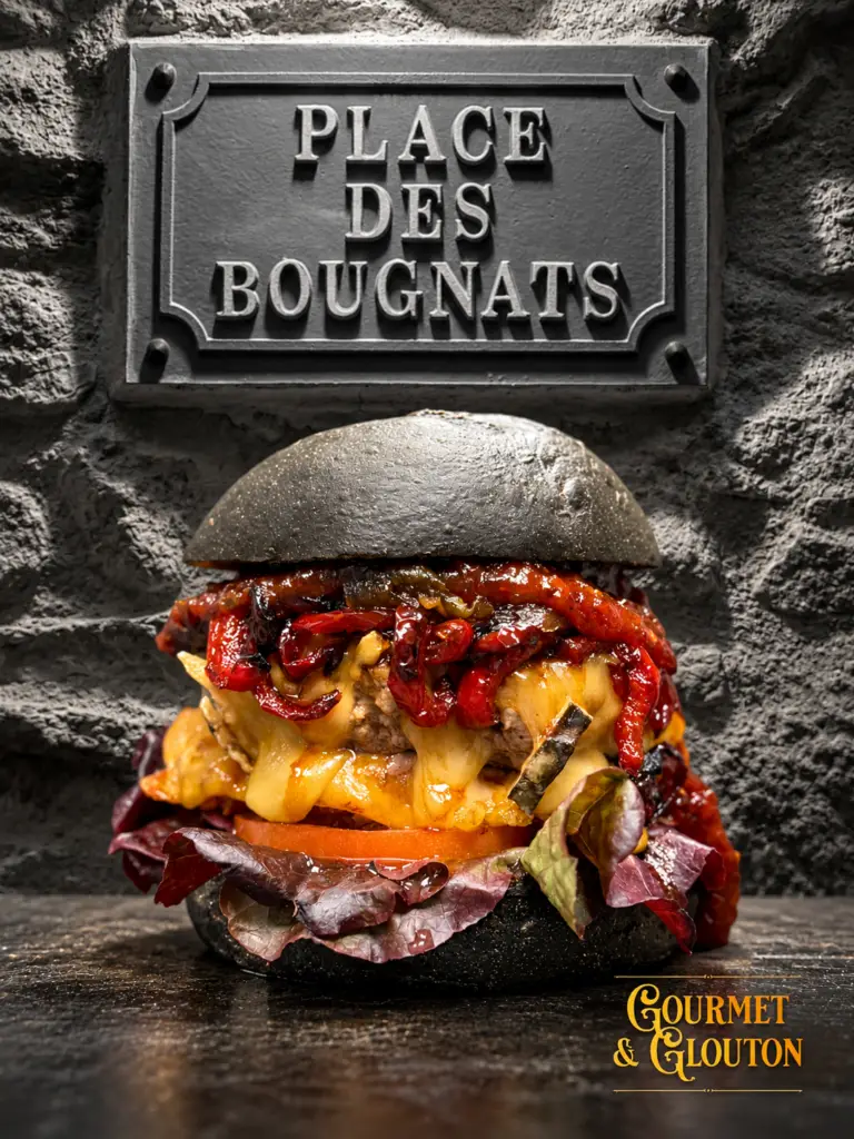 Burger Noir Charbon en couleur devant la plaque « Place des Bougnats » et un mur en pierre en noir et blanc.