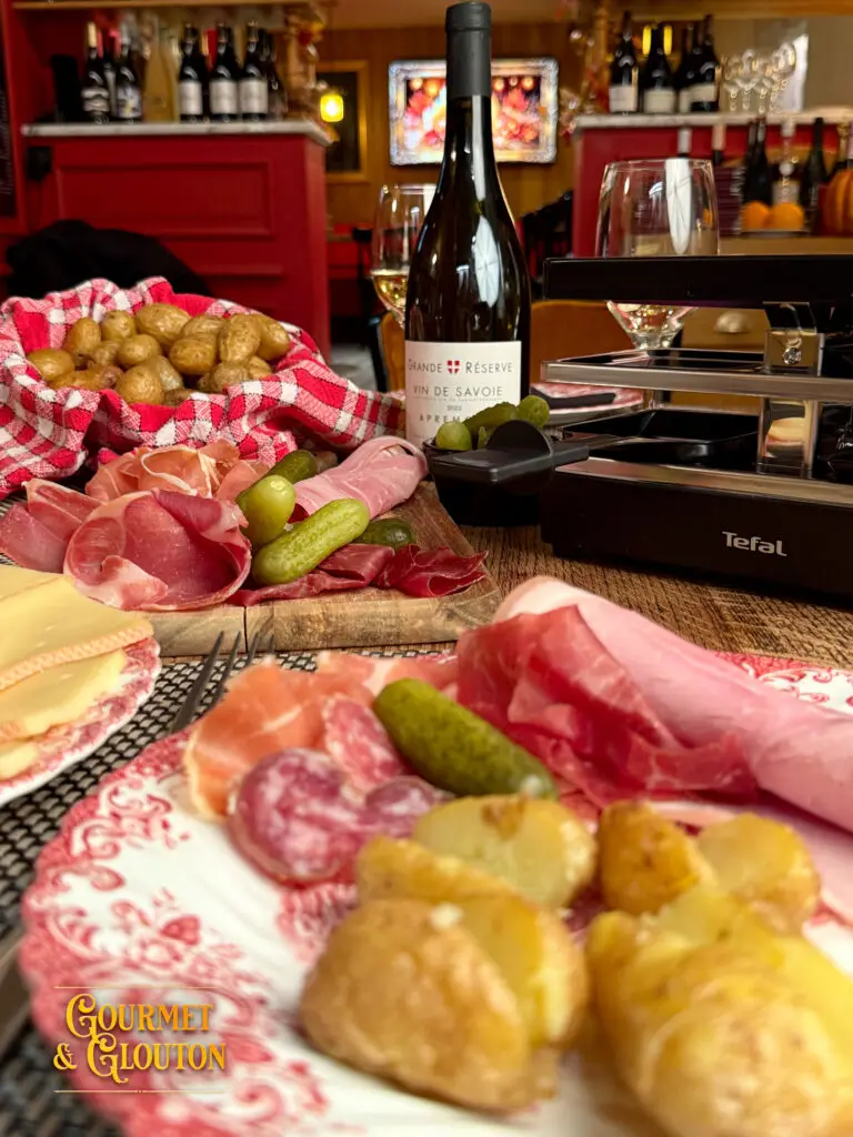 Charcuteries, pommes de terre, fromage à raclette et bouteille d’Apremont sur une table chez Gourmet & Glouton.