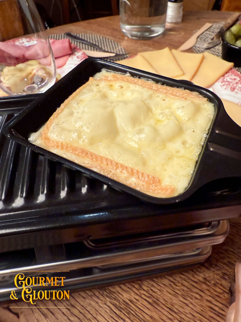 Fromage à raclette fondu et doré dans son poêlon chez Gourmet & Glouton à Chaudes-Aigues.