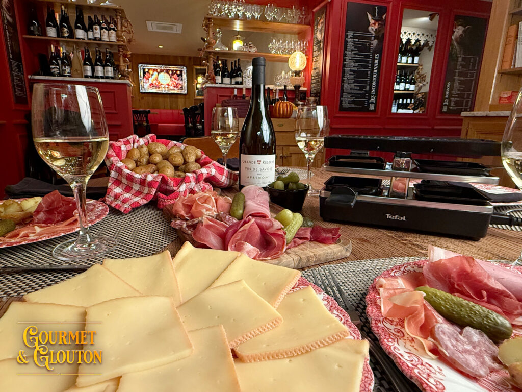 Fromage à raclette, charcuteries, pommes de terre et appareil à raclette sur une table chez Gourmet & Glouton à Chaudes-Aigues.